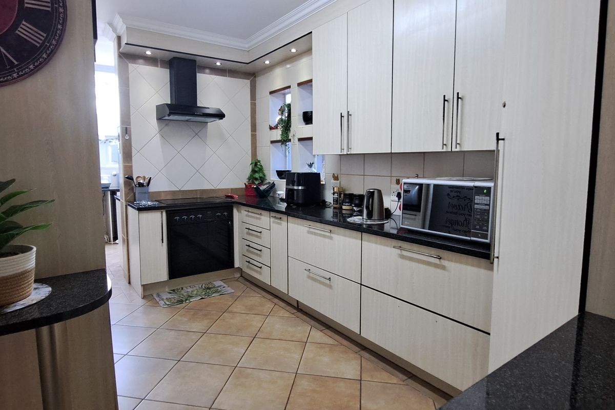 A well-maintained kitchen featuring light-toned cabinetry, dark granite countertops, built-in oven, extractor fan, and ceramic tile flooring with recessed lighting.