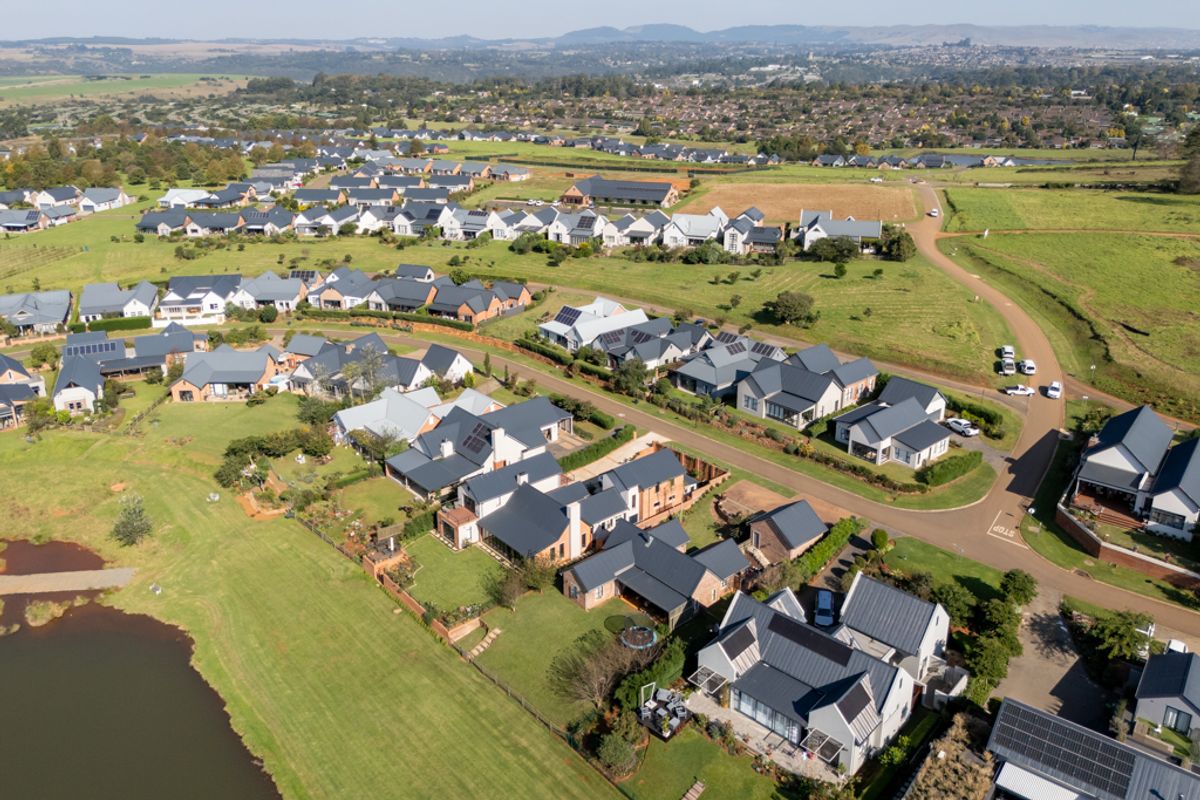 An aerial view of a well-maintained residential estate featuring modern homes, paved streets, green spaces, and a nearby lake.
