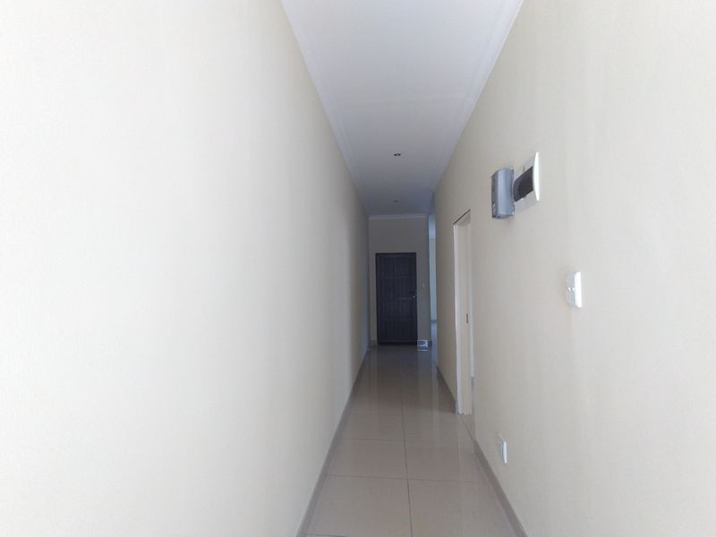 A clean, neutral-toned hallway featuring tiled flooring, recessed lighting, and access to adjacent rooms.