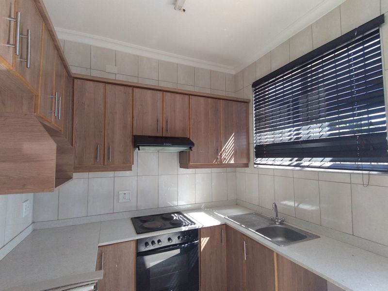 A functional kitchen featuring wood-finish cabinetry, a built-in electric oven and hob, extractor fan, and a double sink with tiled backsplash.