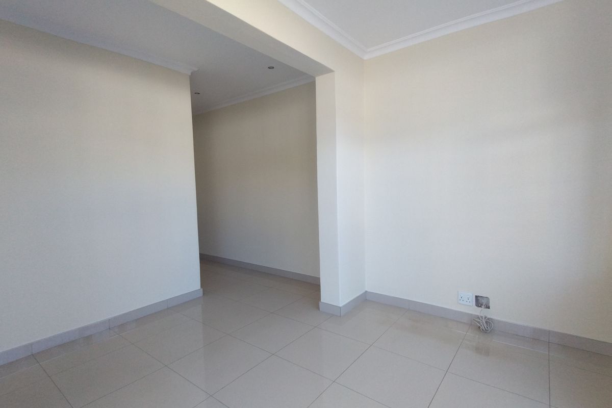 An empty, open-plan living area featuring neutral tiled flooring, recessed downlighting, and coved cornicing, providing a clean canvas for interior design.