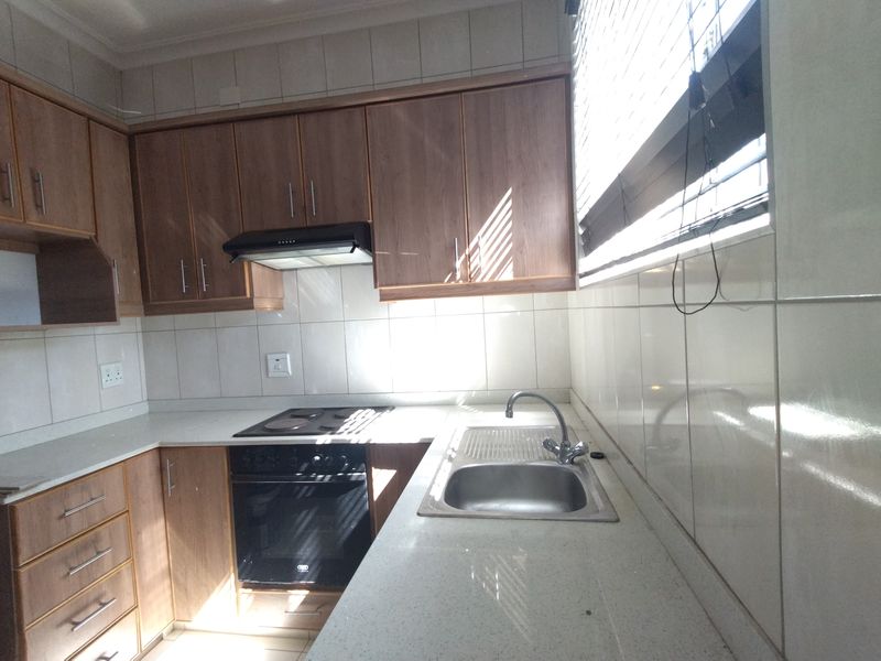 A functional kitchen featuring laminate cabinetry, stone countertops, a built-in oven with hob, and a stainless steel sink with tiled backsplash.