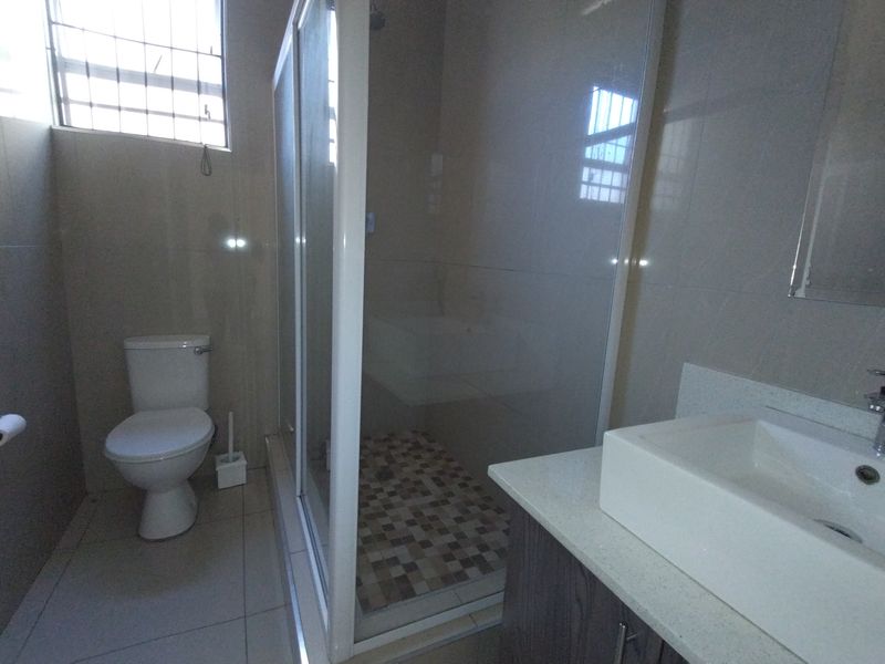 A clean, functional bathroom featuring a glass-enclosed shower, modern vessel sink with vanity cabinet, and neutral floor tiling.