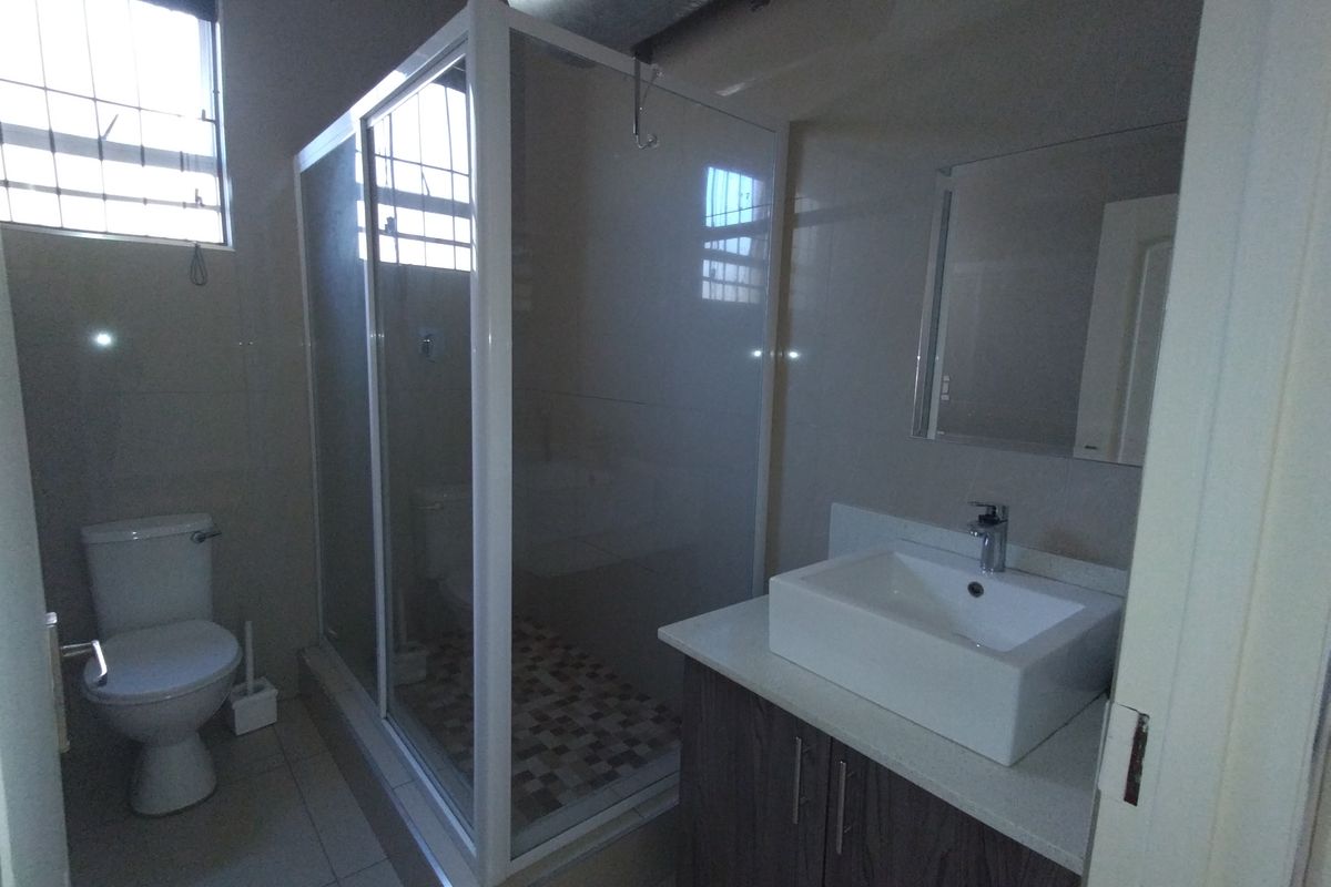 A clean, modern bathroom featuring a glass shower enclosure, a contemporary vessel sink with vanity storage, and neutral wall tiling.