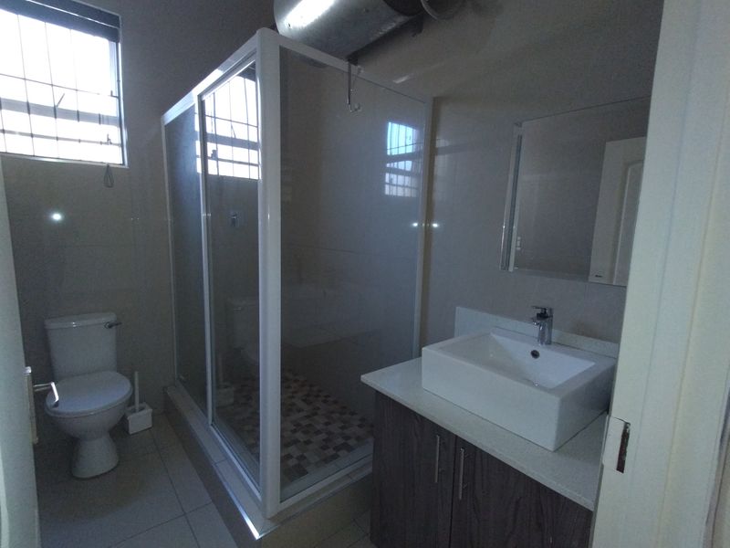 A clean, modern bathroom featuring a glass shower enclosure, a contemporary vessel sink with vanity storage, and neutral wall tiling.