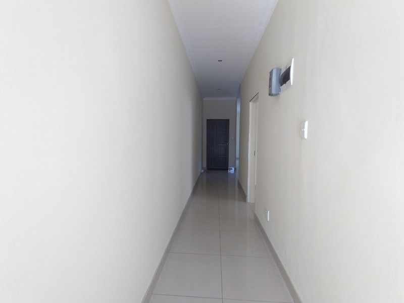 A clean, neutral-toned hallway featuring tiled flooring and recessed downlighting, providing a simple transition between rooms in the apartment.