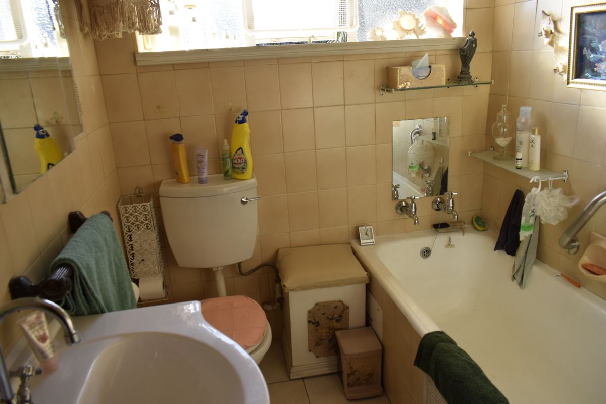 A compact bathroom featuring a bathtub, wall-mounted basin, and toilet with dated wall tiling and chrome fixtures.