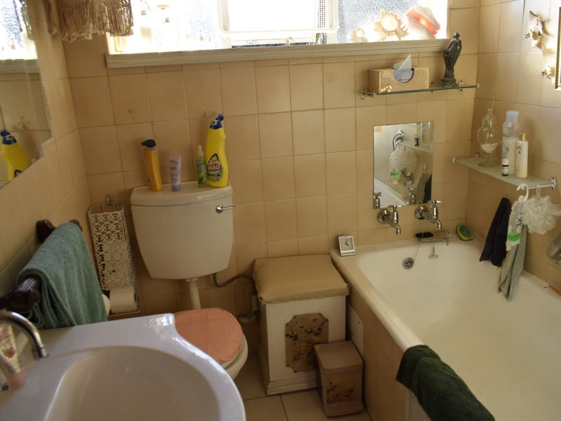 A compact bathroom featuring a bathtub, wall-mounted basin, and toilet with dated wall tiling and chrome fixtures.