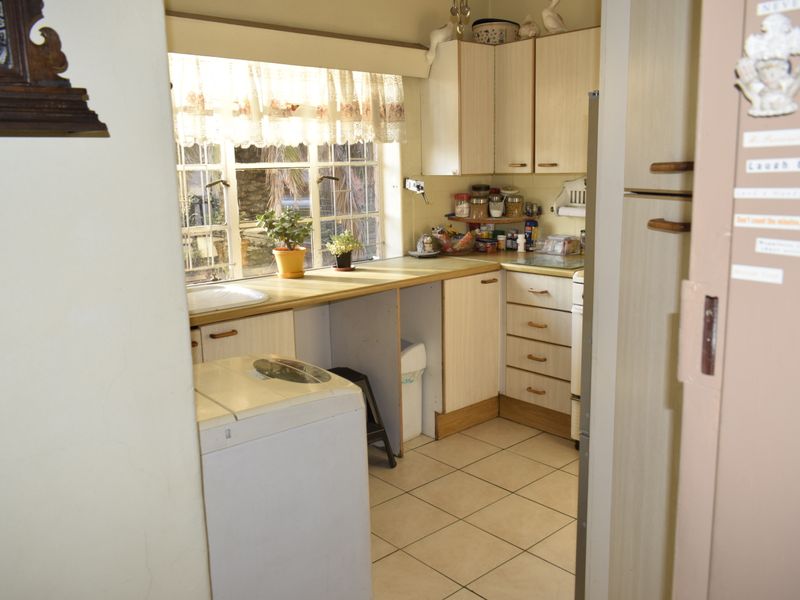A functional kitchen featuring laminate cabinetry, tiled flooring, and a window with burglar bars, offering a practical layout with potential for modern updates.