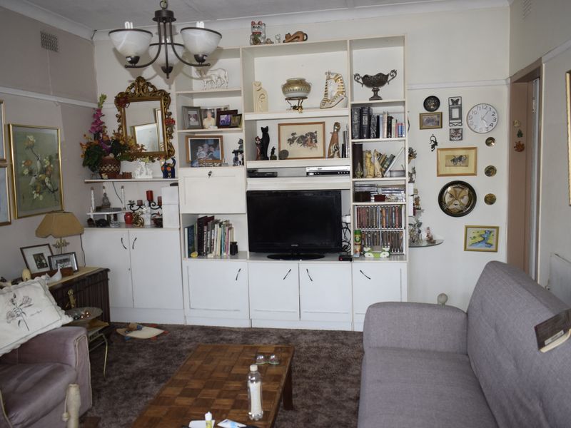 A living room featuring built-in cabinetry and a ceiling light fixture, showing signs of wear including peeling wallpaper and dated carpeting.
