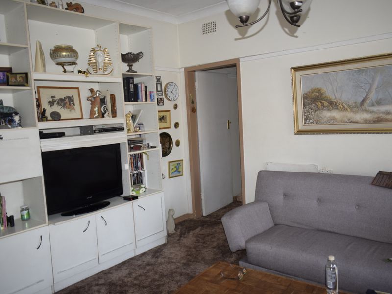 A living room featuring a large built-in white shelving unit, traditional coving, and carpeted flooring.