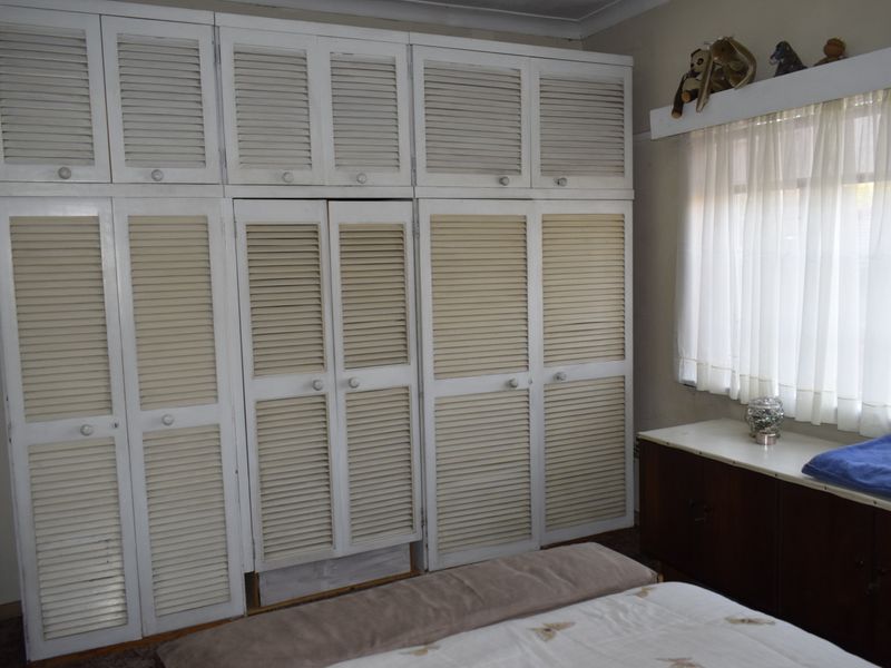 Bedroom featuring extensive floor-to-ceiling built-in cupboards with louvered doors and a window with a curtain rail.