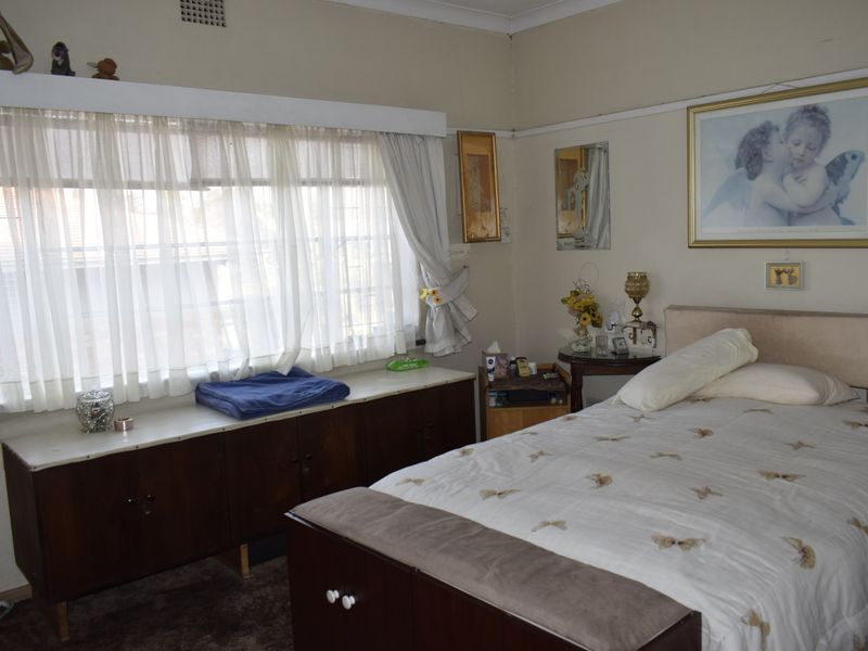 A bedroom featuring built-in cabinetry, window security bars, and traditional cornice detailing, offering a functional space with potential for modernization.
