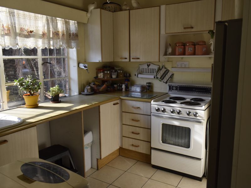 A dated kitchen featuring laminate cabinetry, tiled flooring, and a freestanding electric stove, offering potential for a modern renovation.