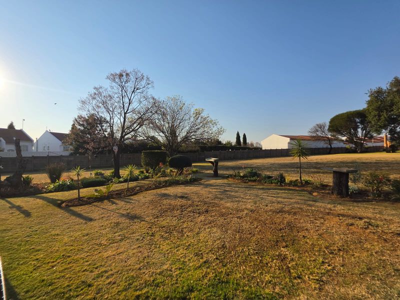 A spacious, open backyard garden featuring established trees, landscaped garden beds, and a perimeter boundary wall, offering potential for further outdoor development.
