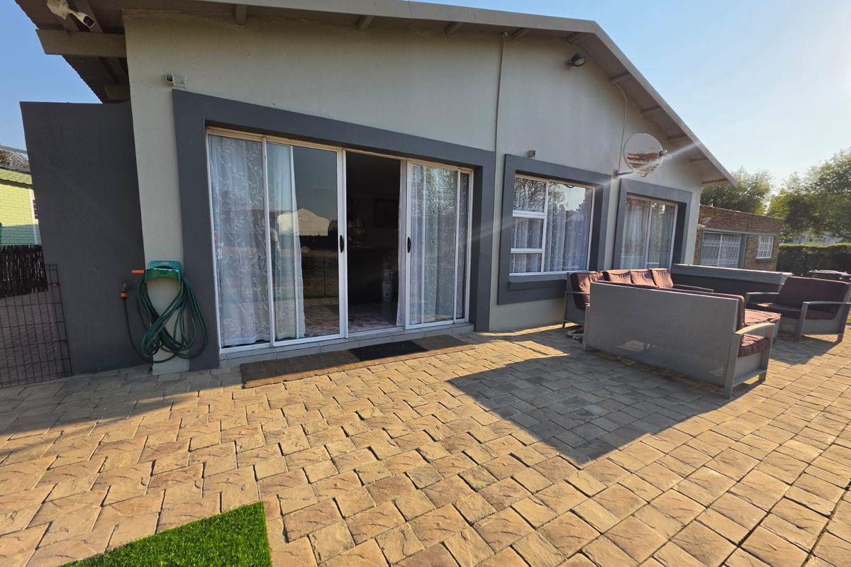 Rear exterior view featuring a paved patio area, sliding glass doors providing access to the interior, and modern aluminium window frames.