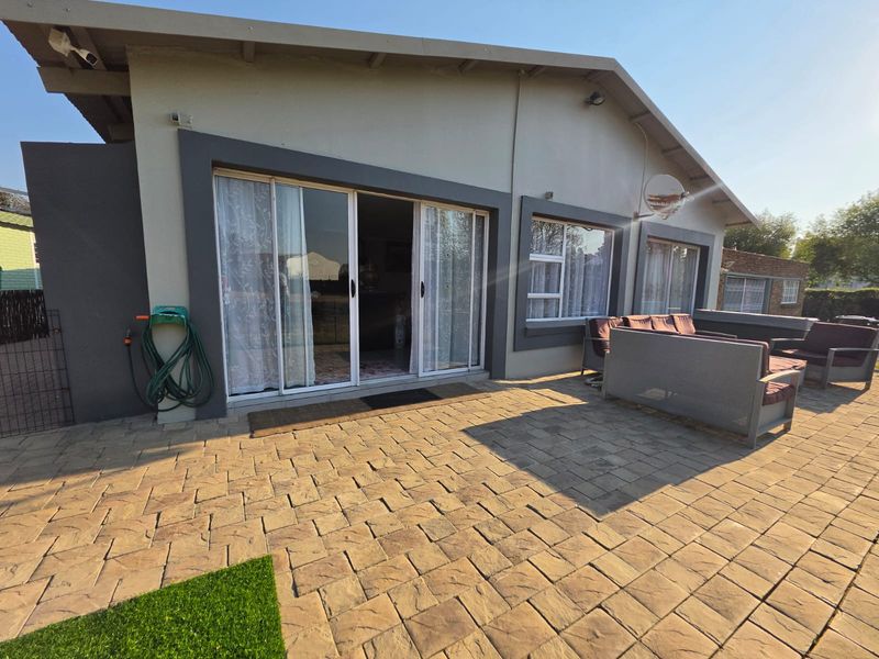 Rear exterior view featuring a paved patio area, sliding glass doors providing access to the interior, and modern aluminium window frames.