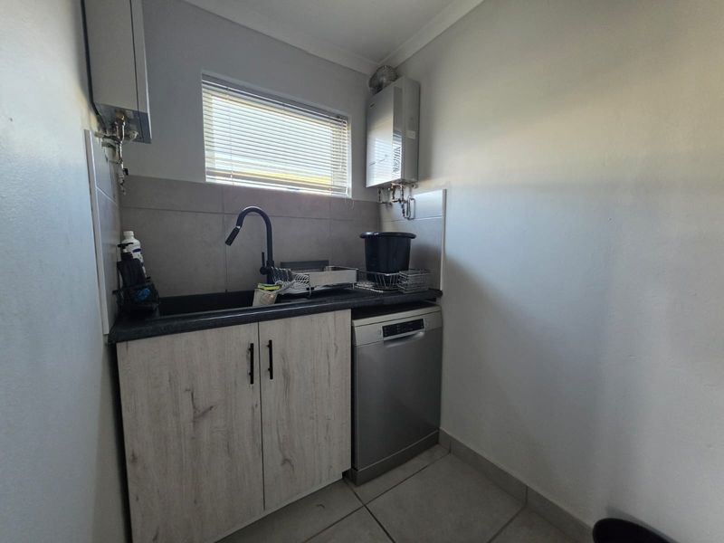 A functional laundry area featuring built-in cabinetry, a sink with a modern mixer tap, tiled splashback, and a wall-mounted gas geyser.