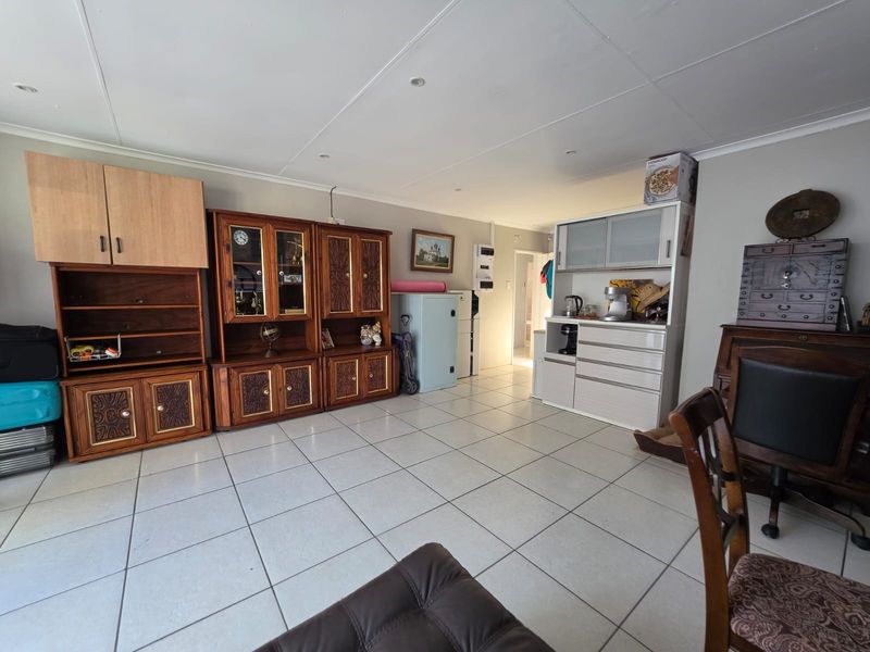 A spacious living area featuring neutral tiled flooring and recessed ceiling lighting, offering a versatile layout for various furniture arrangements.