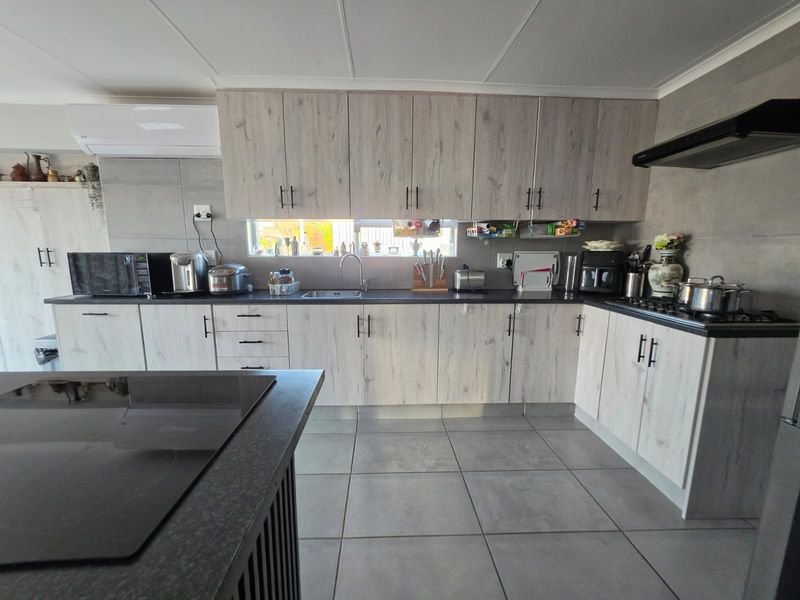 Modern kitchen featuring light wood-grain cabinetry, dark countertops, tiled flooring, integrated gas hob, extractor fan, and a functional layout with ample storage.