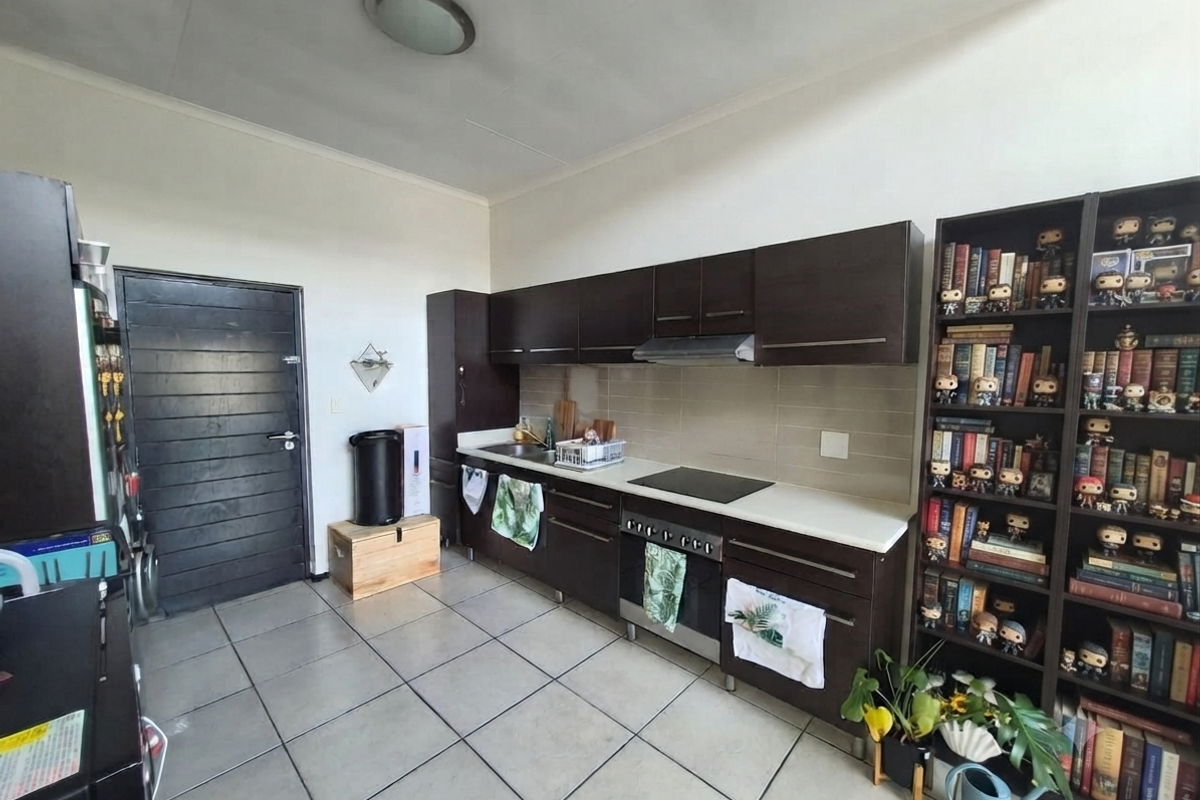 A functional kitchen featuring dark wood cabinetry, built-in oven, electric hob, extractor fan, and tiled flooring with a neutral backsplash.