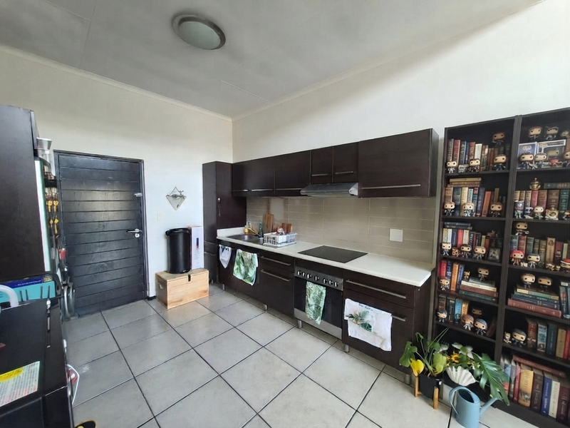 A functional kitchen featuring dark wood cabinetry, built-in oven, electric hob, extractor fan, and tiled flooring with a neutral backsplash.