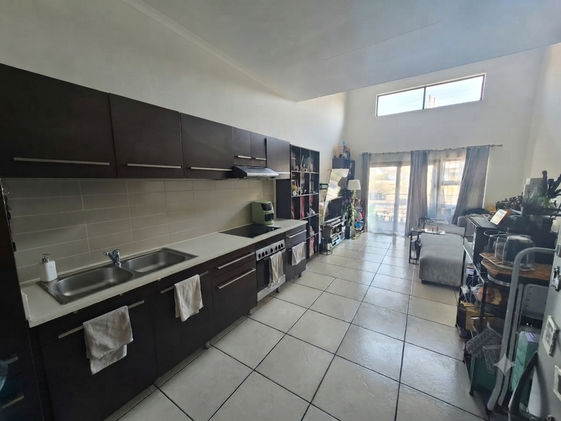 Spacious open-plan kitchen and living area featuring dark wood cabinetry, built-in appliances, tiled flooring, and high ceilings with natural light from sliding doors.