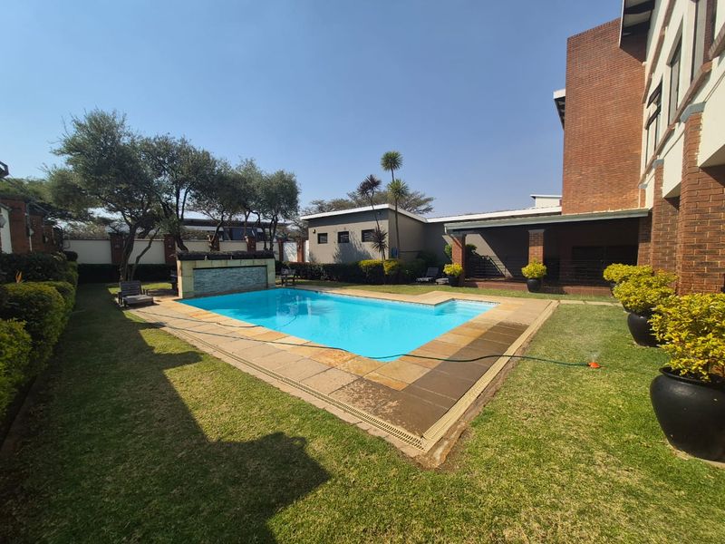 A well-maintained outdoor pool area featuring a built-in water feature, stone coping, and a spacious garden setting adjacent to the main building structure.