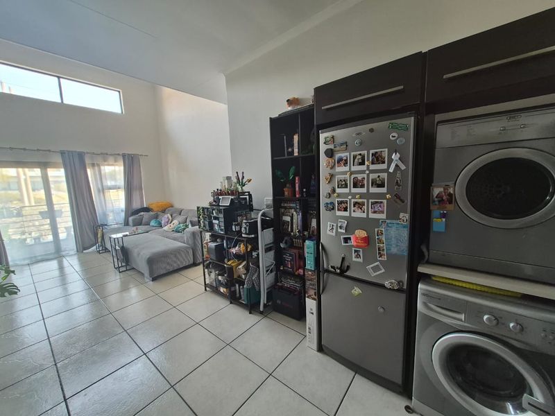 Open-plan living area featuring tiled flooring, high ceilings, and a sliding glass door leading to an outdoor space, with integrated laundry and kitchen cabinetry.