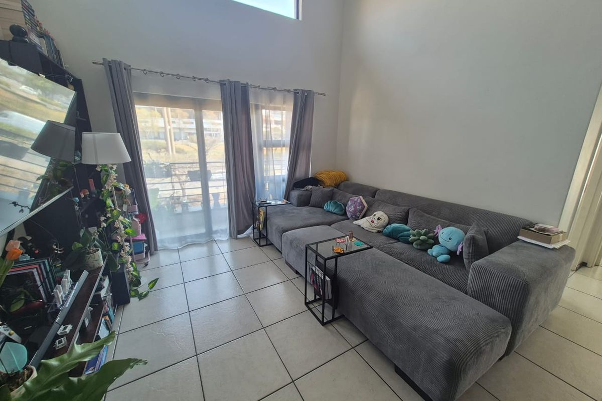 Spacious living room featuring high double-volume ceilings, large sliding glass doors providing natural light, and neutral tiled flooring.
