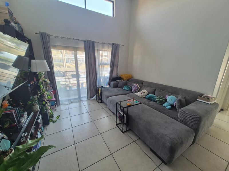 Spacious living room featuring high double-volume ceilings, large sliding glass doors providing natural light, and neutral tiled flooring.