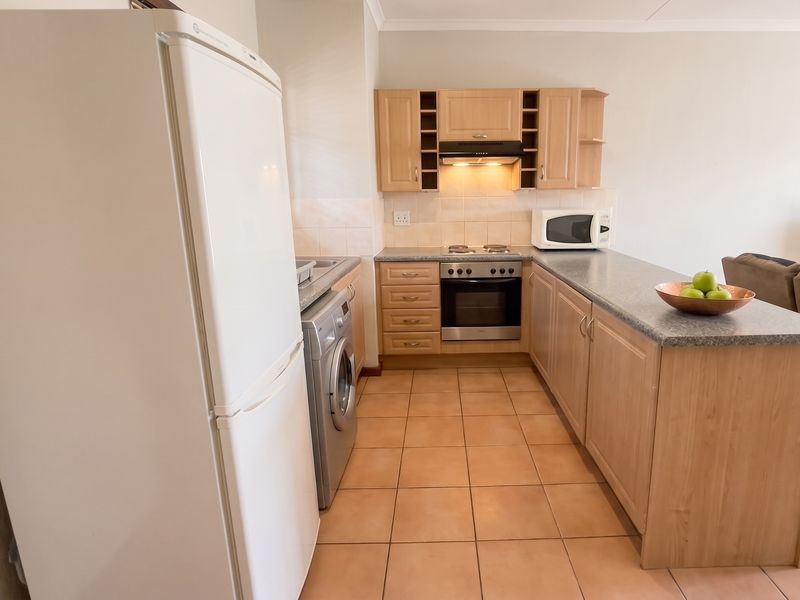 A functional kitchen featuring light wood cabinetry, laminate countertops, a breakfast bar, and tiled flooring, integrated with a living area.