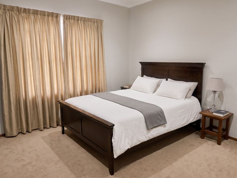 A well-maintained bedroom featuring neutral wall tones, carpeted flooring, and floor-to-ceiling curtains.