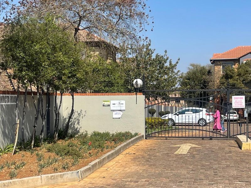 View of the residential complex entrance featuring a secure gated access point, perimeter wall, and paved driveway.