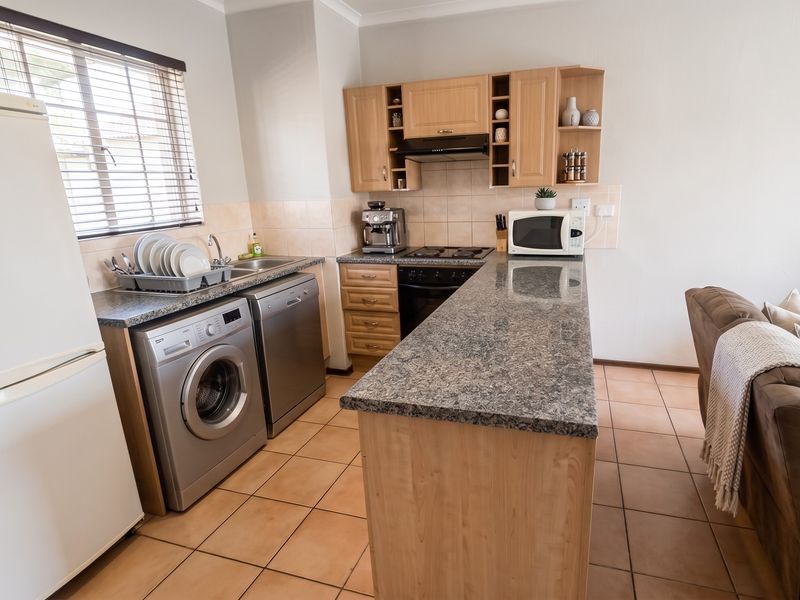 A functional kitchen featuring wooden cabinetry, granite countertops, a tiled backsplash, and integrated appliances, seamlessly connected to the living area.
