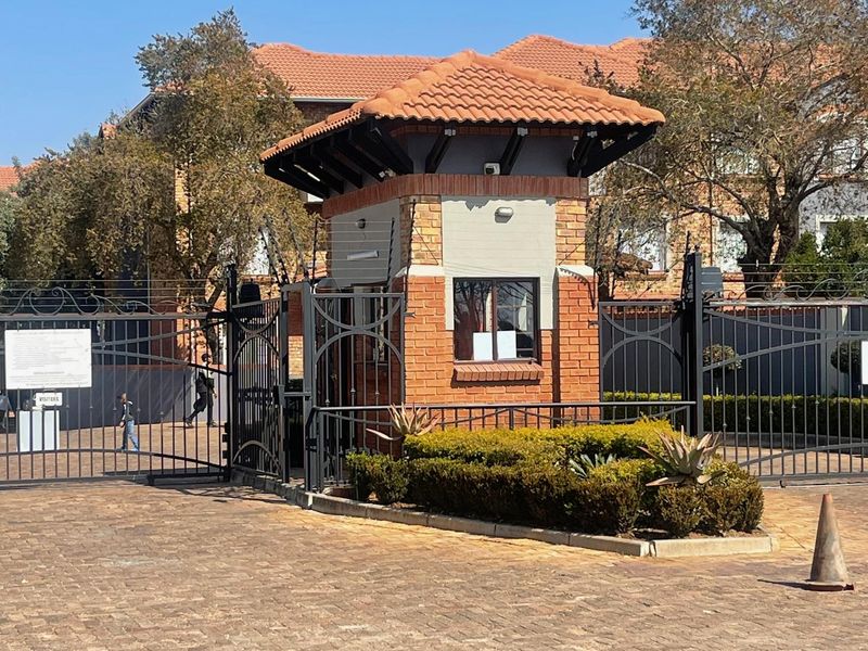 A secure gated entrance to the apartment complex featuring a brick guard house, wrought iron gates, and electric fencing.