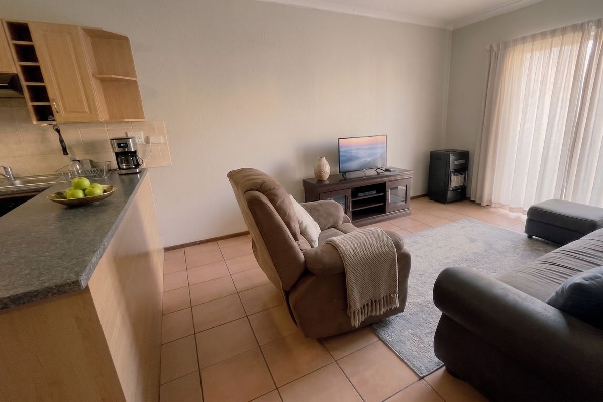 Open-plan living area featuring tiled flooring, a functional kitchen with laminate cabinetry, and direct access to a patio through sliding glass doors.