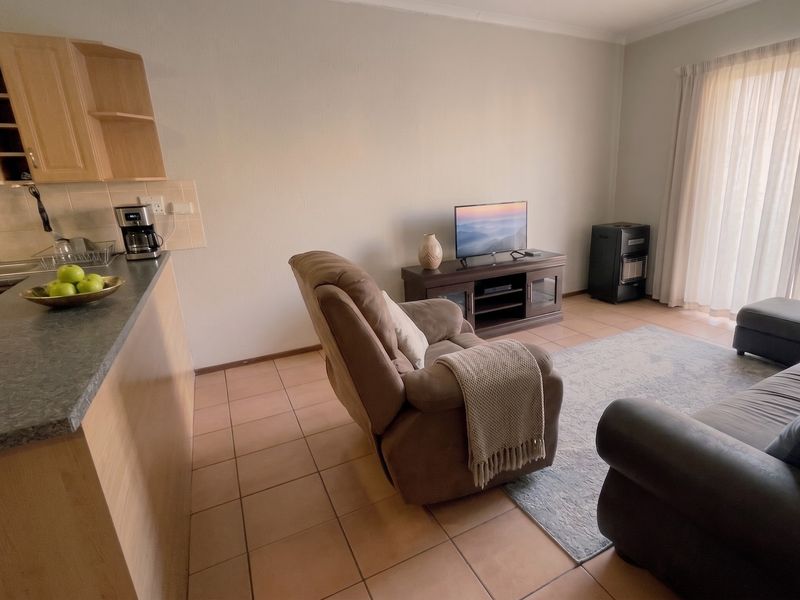 Open-plan living area featuring tiled flooring, a functional kitchen with laminate cabinetry, and direct access to a patio through sliding glass doors.