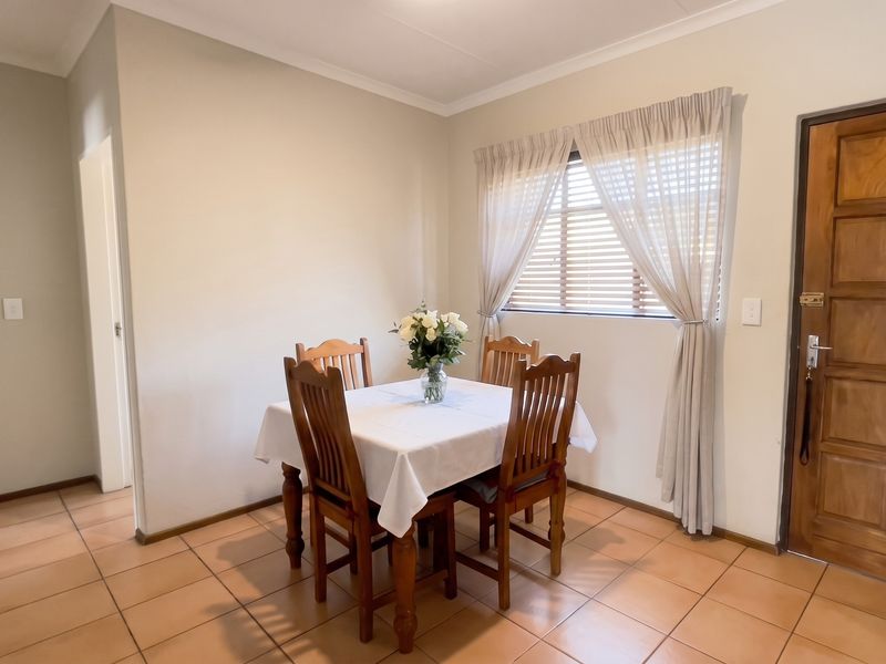 A dining area featuring tiled flooring, a wooden panel door, and natural light through a window with venetian blinds.