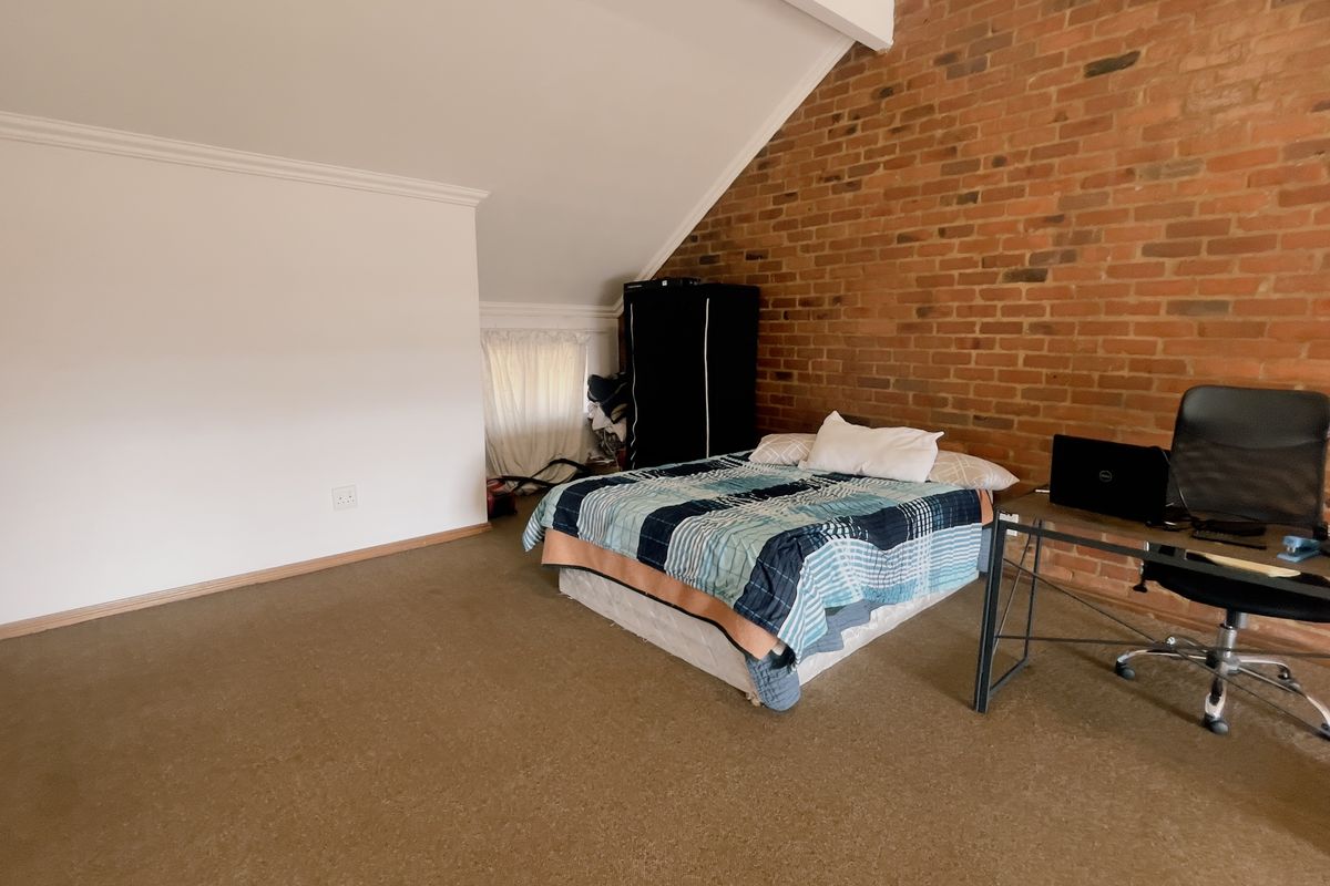 Spacious bedroom featuring an exposed brick feature wall, sloped ceiling, and carpeted flooring, offering a unique architectural character.