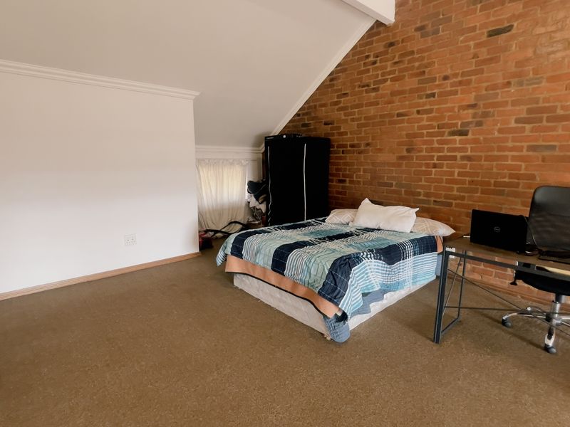 Spacious bedroom featuring an exposed brick feature wall, sloped ceiling, and carpeted flooring, offering a unique architectural character.