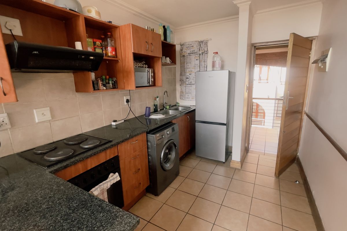 A functional kitchen featuring wood-finish cabinetry, granite countertops, an electric hob, and an integrated laundry space, with direct access to an outdoor area.