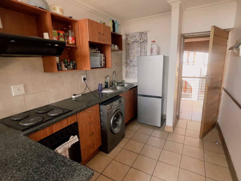A functional kitchen featuring wood-finish cabinetry, granite countertops, an electric hob, and an integrated laundry space, with direct access to an outdoor area.