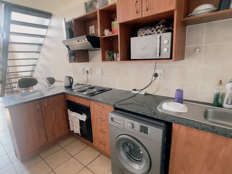 A functional kitchen featuring wooden cabinetry, granite countertops, built-in oven and hob, and tiled flooring, with an adjacent staircase leading to an upper level.