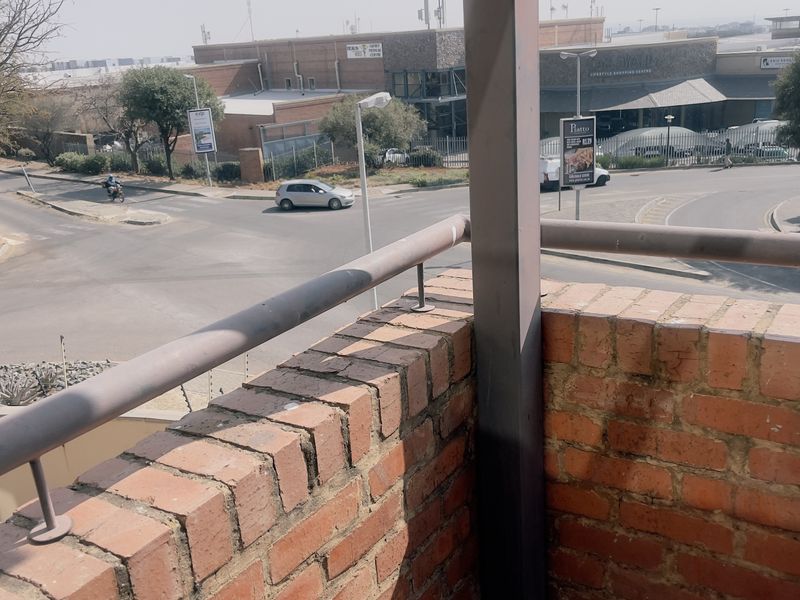 A balcony featuring a brick parapet wall and metal railing, overlooking a street intersection and nearby commercial area.