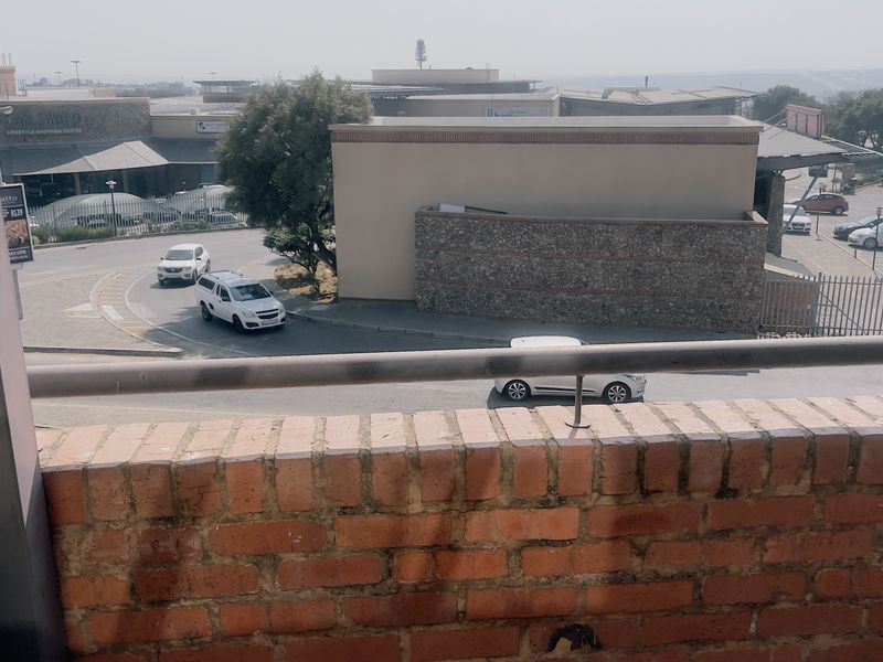 A balcony featuring a brick parapet wall and metal railing, offering an elevated view of the surrounding street and commercial area.