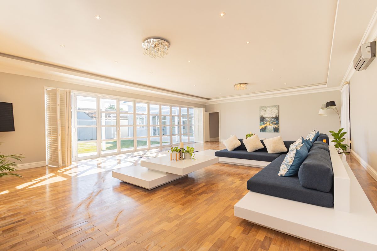 Spacious living room featuring polished parquet flooring, elegant cove molding, recessed lighting, and expansive bi-fold glass doors providing seamless access to the outdoor area.