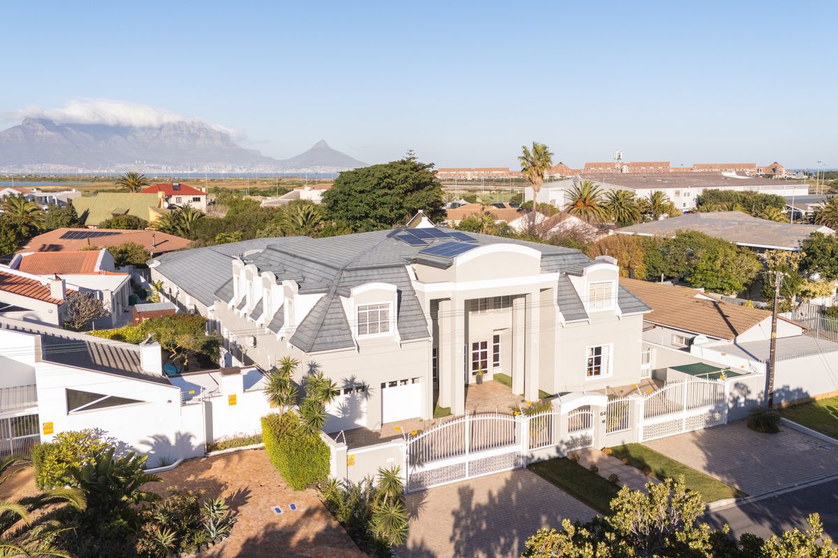Aerial view of a large, well-maintained double-story residence featuring a tiled roof with solar panels, paved driveway, and secure perimeter fencing.