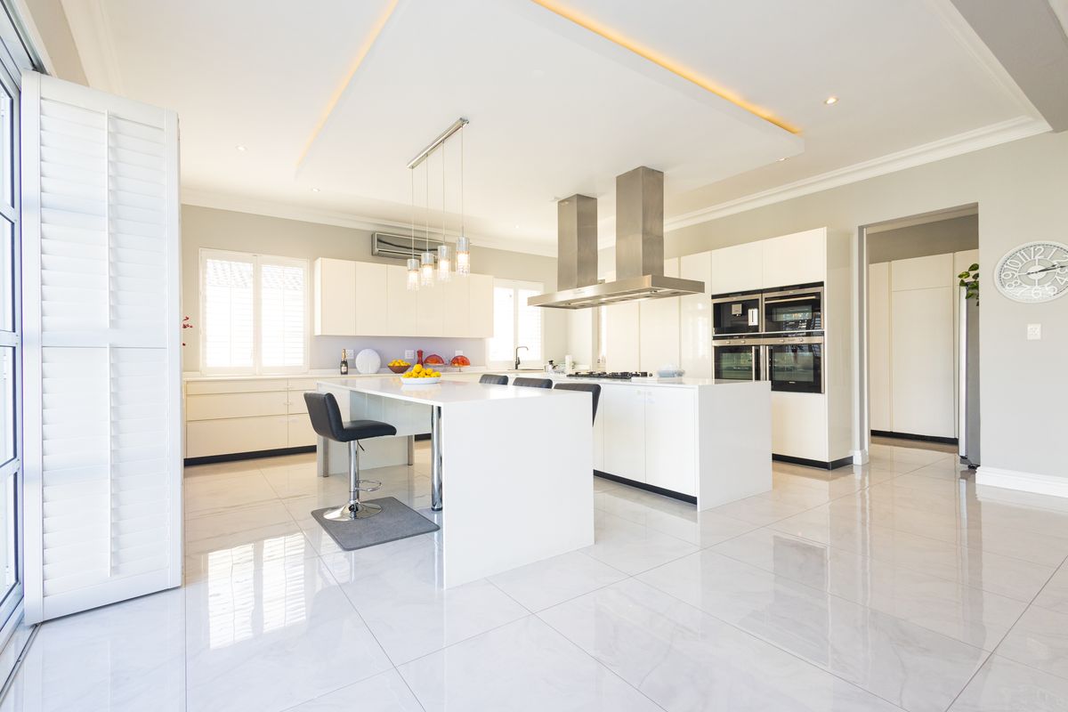 Modern, high-end kitchen featuring a large central island, integrated stainless steel appliances, sleek cabinetry, and polished porcelain flooring under a recessed ceiling.