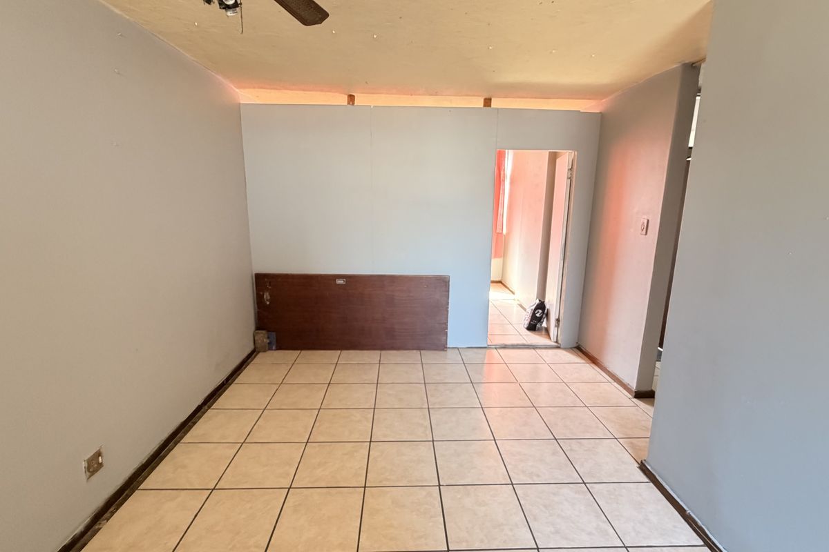 An empty living area featuring ceramic floor tiles, a ceiling fan, and an unfinished partition wall leading to an adjacent room.